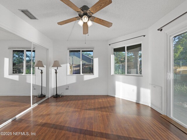 interior space featuring wood finished floors, visible vents, a ceiling fan, baseboards, and a textured ceiling