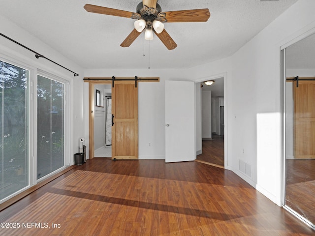 unfurnished room with a barn door, wood finished floors, visible vents, baseboards, and ceiling fan