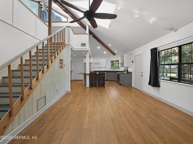 unfurnished living room with lofted ceiling with beams, light wood-type flooring, visible vents, stairs, and ceiling fan