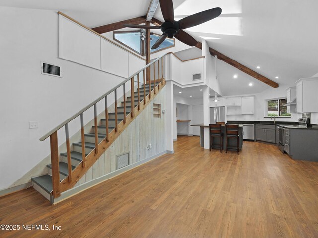 unfurnished living room featuring a ceiling fan, visible vents, beam ceiling, and light wood-style flooring