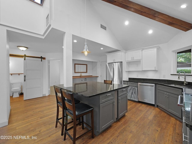 kitchen with a barn door, vaulted ceiling with beams, a sink, appliances with stainless steel finishes, and white cabinetry