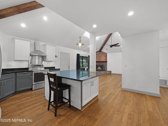 kitchen with a ceiling fan, dark countertops, lofted ceiling with beams, stainless steel electric range oven, and wall chimney exhaust hood