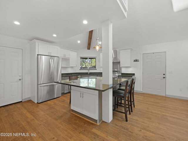 kitchen with white cabinets, stainless steel appliances, dark countertops, wood finished floors, and wall chimney range hood