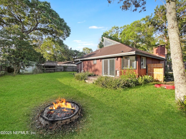 back of property featuring a chimney, fence, an outdoor fire pit, and a lawn