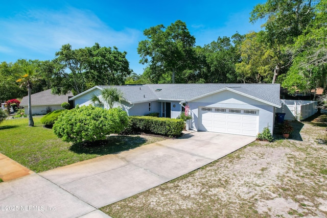 ranch-style home with fence, a shingled roof, concrete driveway, an attached garage, and a front yard