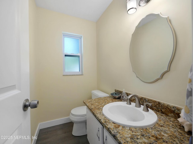 half bath featuring baseboards, wood finished floors, vanity, and toilet