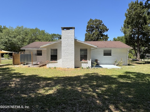 rear view of property featuring a lawn, a chimney, a patio, brick siding, and roof with shingles