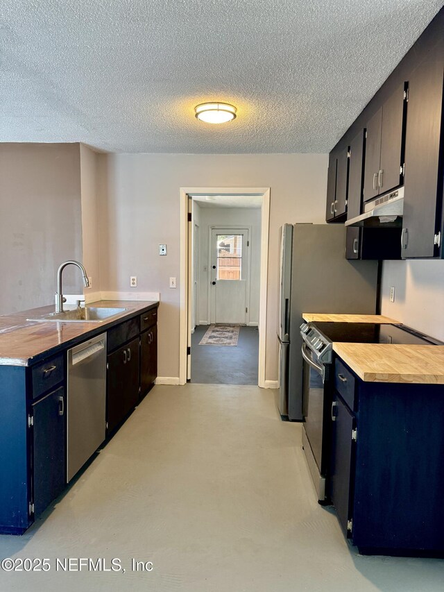 kitchen with a textured ceiling, blue cabinetry, under cabinet range hood, stainless steel appliances, and a sink