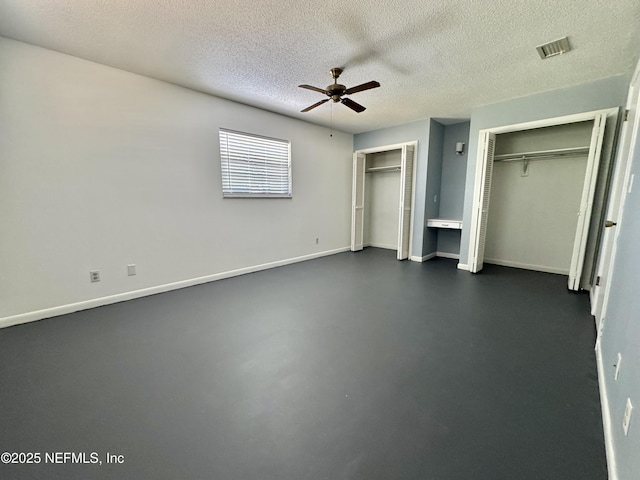 unfurnished bedroom with a textured ceiling, finished concrete floors, visible vents, multiple closets, and baseboards