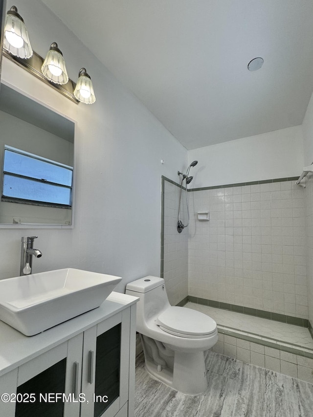 full bathroom featuring vanity, a tile shower, toilet, and wood finished floors