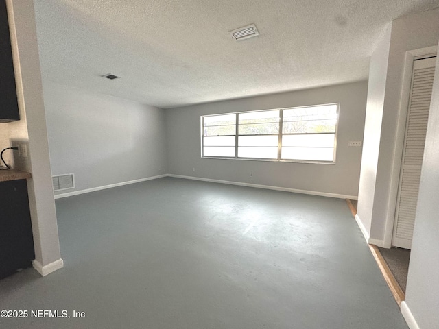 unfurnished living room featuring a textured ceiling, finished concrete floors, baseboards, and visible vents