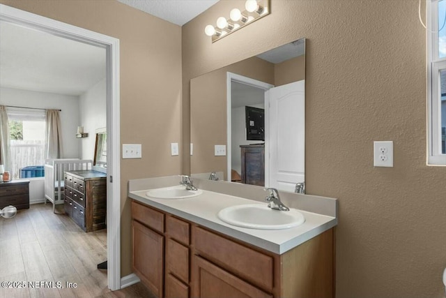bathroom featuring a textured wall, wood finished floors, a sink, and double vanity
