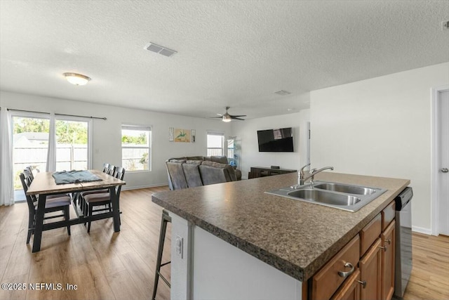 kitchen featuring brown cabinets, light wood finished floors, visible vents, stainless steel dishwasher, and a sink