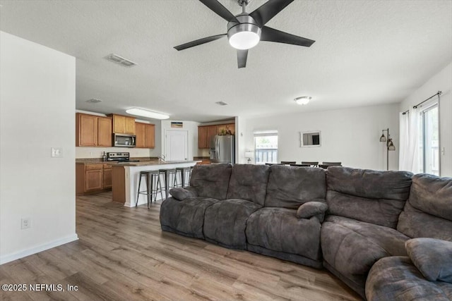 living area featuring light wood-style floors, visible vents, a wealth of natural light, and ceiling fan