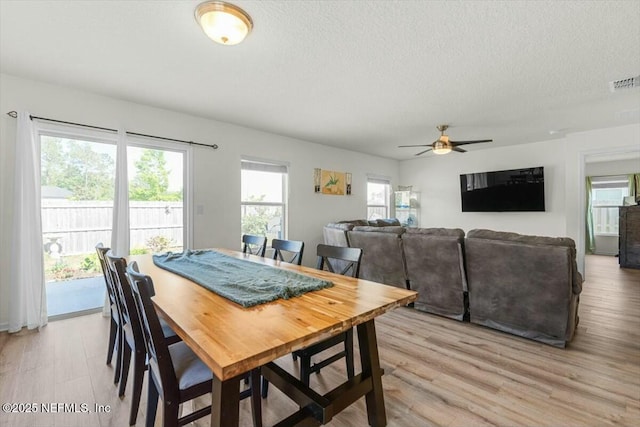 dining space with ceiling fan, a textured ceiling, visible vents, and light wood-style flooring