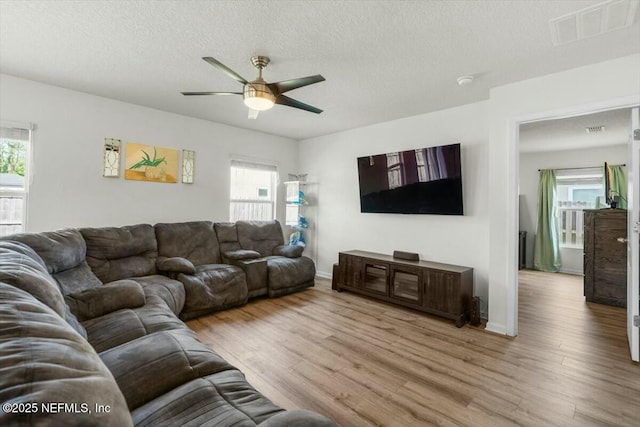 living area with wood finished floors, plenty of natural light, a ceiling fan, and visible vents