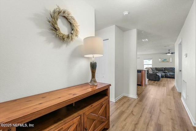 hallway with baseboards, a textured ceiling, and light wood finished floors