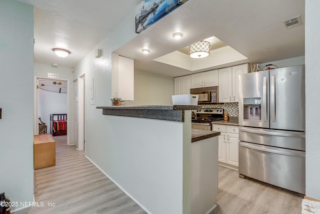 kitchen with dark countertops, white cabinets, stainless steel appliances, and light wood-style flooring