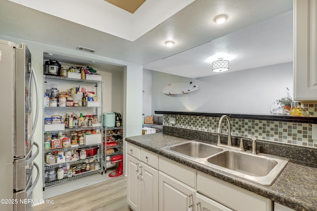 kitchen featuring dark countertops, a sink, freestanding refrigerator, tasteful backsplash, and visible vents