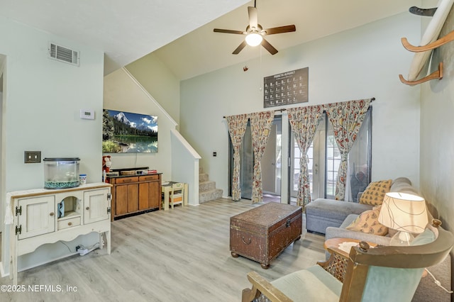 living room featuring a ceiling fan, a towering ceiling, visible vents, wood finished floors, and stairs