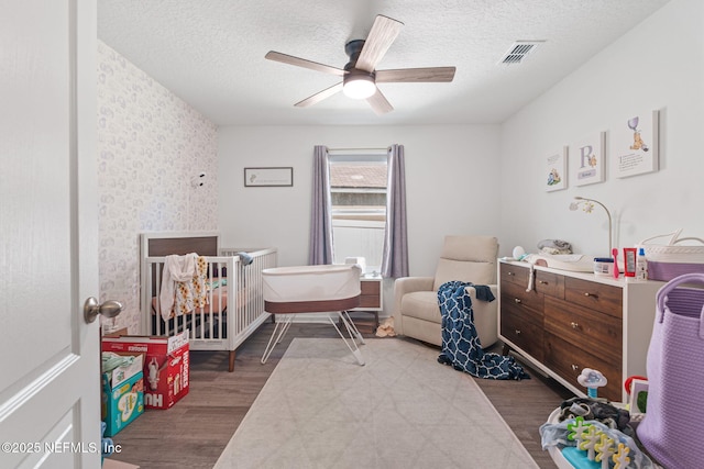 2916 Duck Hollow Ln, Green Cove Springs, FL 32043 - bedroom featuring wood finished floors, a crib, a textured ceiling, a ceiling fan, and wallpapered walls