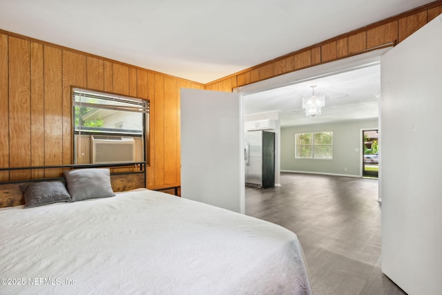 bedroom featuring freestanding refrigerator, cooling unit, wood walls, a notable chandelier, and baseboards