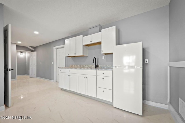 kitchen with freestanding refrigerator, marble finish floor, baseboards, white cabinetry, and a sink