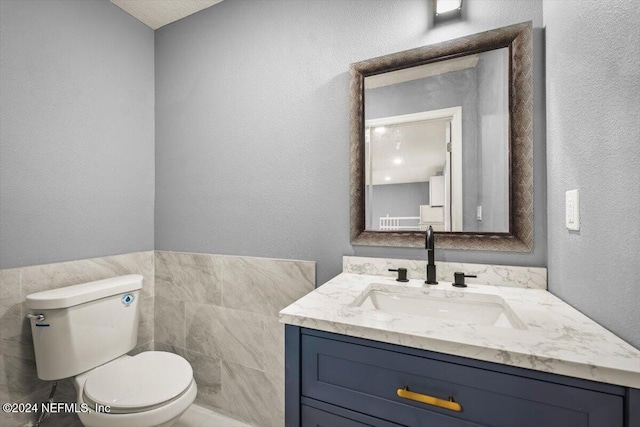 bathroom featuring vanity, a textured wall, toilet, and tile walls
