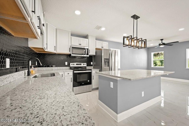 kitchen with decorative backsplash, a center island, white cabinetry, a sink, and appliances with stainless steel finishes