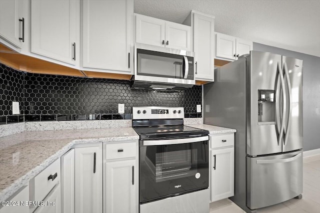 kitchen featuring stainless steel appliances, light stone countertops, white cabinetry, and tasteful backsplash