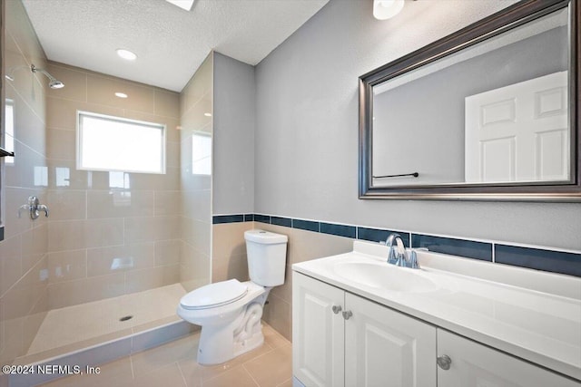bathroom featuring vanity, toilet, a textured ceiling, tile walls, and tiled shower