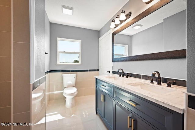 full bath featuring double vanity, a sink, toilet, and tile walls