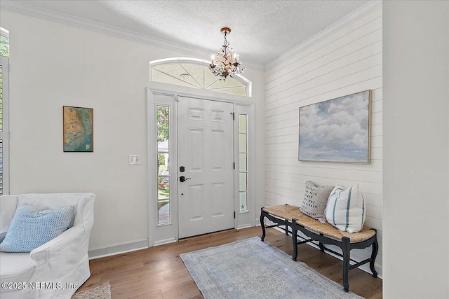 entrance foyer featuring wood walls, wood finished floors, ornamental molding, a textured ceiling, and a notable chandelier