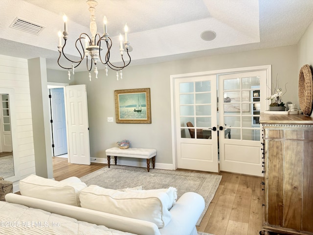 living room with a textured ceiling, light wood-style flooring, visible vents, and an inviting chandelier