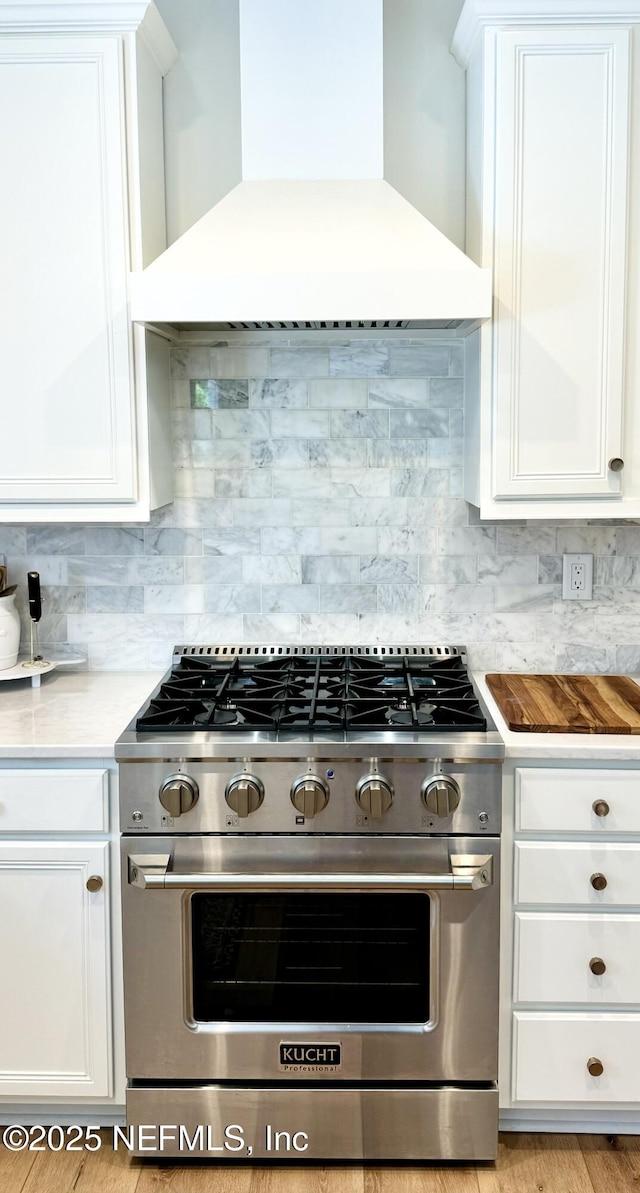 kitchen with custom exhaust hood, decorative backsplash, high end stainless steel range, and white cabinetry
