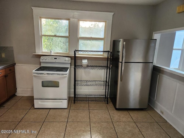 2138 Park St, Jacksonville, FL 32204 - kitchen featuring white electric range oven, light tile patterned floors, a wainscoted wall, and freestanding refrigerator