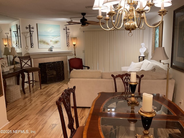dining area with visible vents, wood finished floors, a tiled fireplace, and ceiling fan with notable chandelier