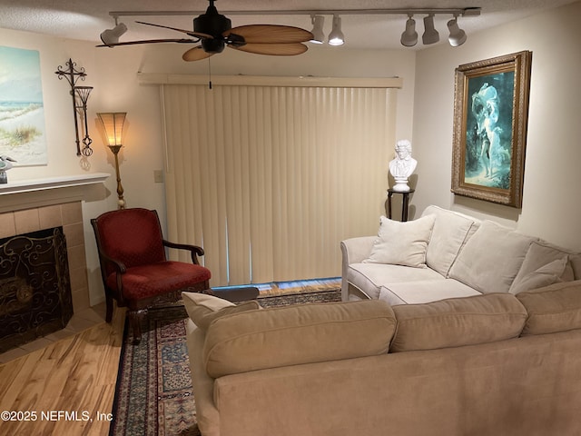 living area with a textured ceiling, a tile fireplace, a ceiling fan, wood finished floors, and track lighting