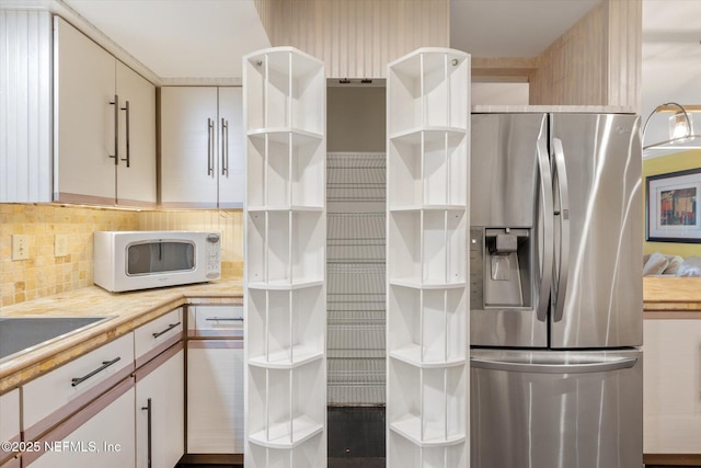 kitchen featuring open shelves, white microwave, stainless steel refrigerator with ice dispenser, light countertops, and backsplash