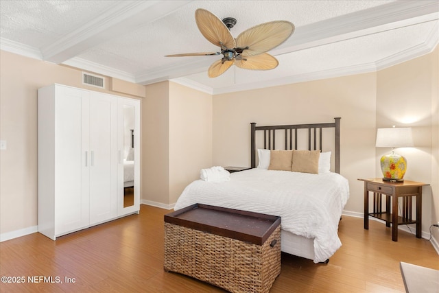 bedroom featuring a textured ceiling, wood finished floors, beamed ceiling, visible vents, and ornamental molding