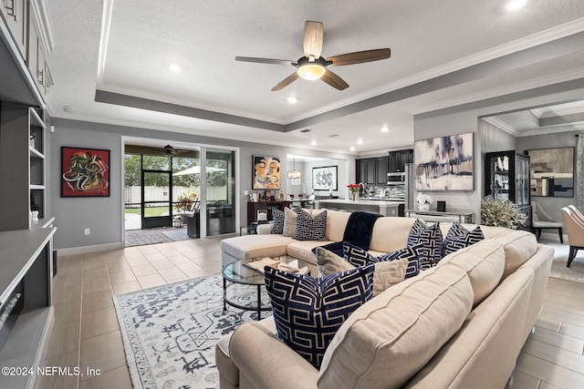 living room featuring a raised ceiling, a ceiling fan, baseboards, and ornamental molding