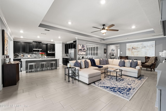 living room featuring a tray ceiling, visible vents, crown molding, and ceiling fan