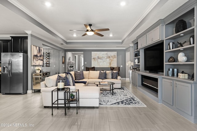 living room with crown molding, a ceiling fan, a glass covered fireplace, and a tray ceiling