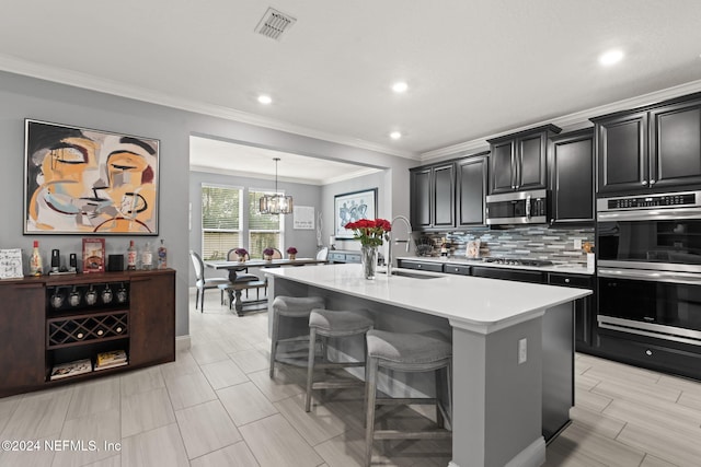 kitchen with dark cabinets, a center island with sink, light countertops, backsplash, and appliances with stainless steel finishes