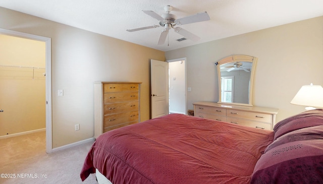 bedroom featuring ceiling fan, light carpet, a walk in closet, baseboards, and visible vents