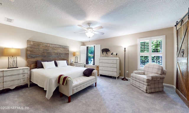 carpeted bedroom with a barn door, a textured ceiling, a ceiling fan, baseboards, and visible vents