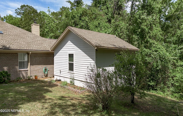 view of property exterior with a shingled roof, a chimney, a yard, and brick siding