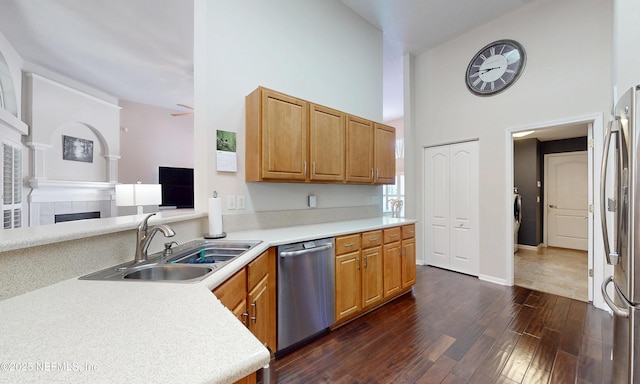 kitchen featuring dark wood-style flooring, a fireplace, a high ceiling, a sink, and appliances with stainless steel finishes