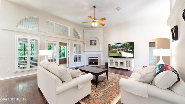 living area featuring a glass covered fireplace, a ceiling fan, baseboards, visible vents, and dark wood-style floors