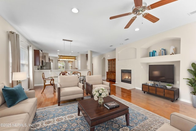 living area with visible vents, baseboards, light wood-type flooring, a ceiling fan, and a fireplace with flush hearth